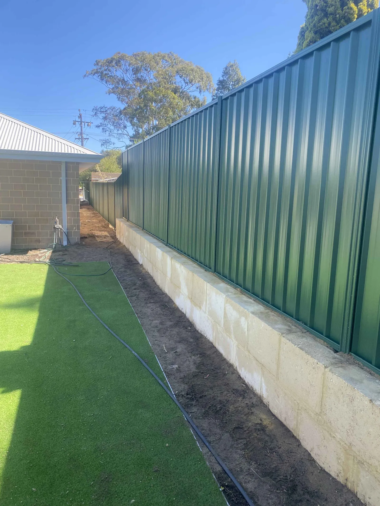 A limestone block retaining wall with a green Colorbond fence built on top, Perth